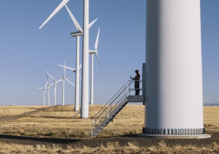 A wind farm technician standing and using a laptop at the base of a turbine on a wind farm in open countryside at Palouse.